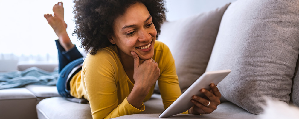 A lady relaxing on the couch using her tablet.